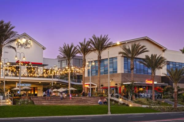 Exterior twilight photo of Pacific City shopping center in Huntington Beach, CA, with palm trees and a blue-purple evening sky