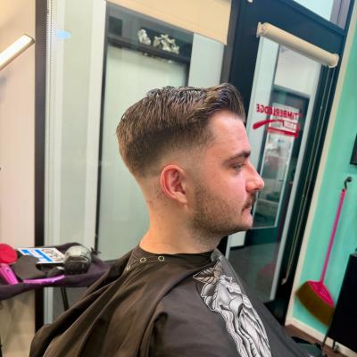 Man with a classic men's fade haircut, short on sides with length on top, wearing a black patterned cape