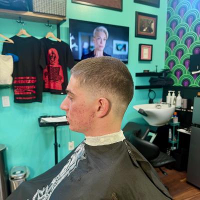 Man with a clean short taper haircut viewed from behind, wearing a black cape, teal barbershop background
