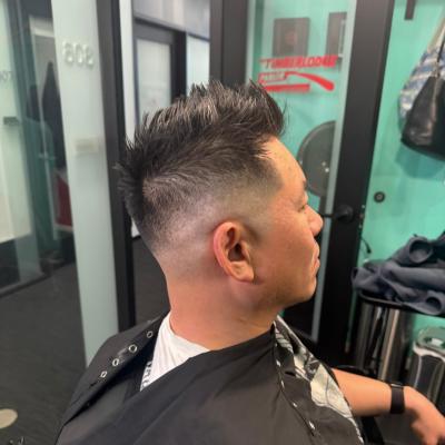 Man with a high skin fade haircut, short dark hair on top, wearing a black cape, profile view
