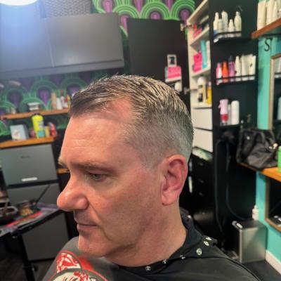 Older man with short silver hair and a fresh cut, wearing a vibrant graphic barber cape, profile view
