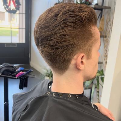 Young man with a short textured crop and clean tapered sides, wearing a black barber cape, viewed from behind in a barbershop