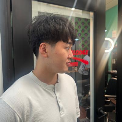 Asian man with a short blunt bowl cut with tapered sides, wearing a gray henley shirt, profile view reflected in barbershop mirror