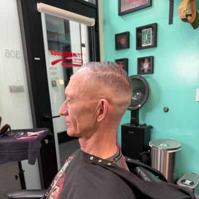 Senior man with a fresh fade haircut, seated in barber chair wearing a black cape, teal wall in background