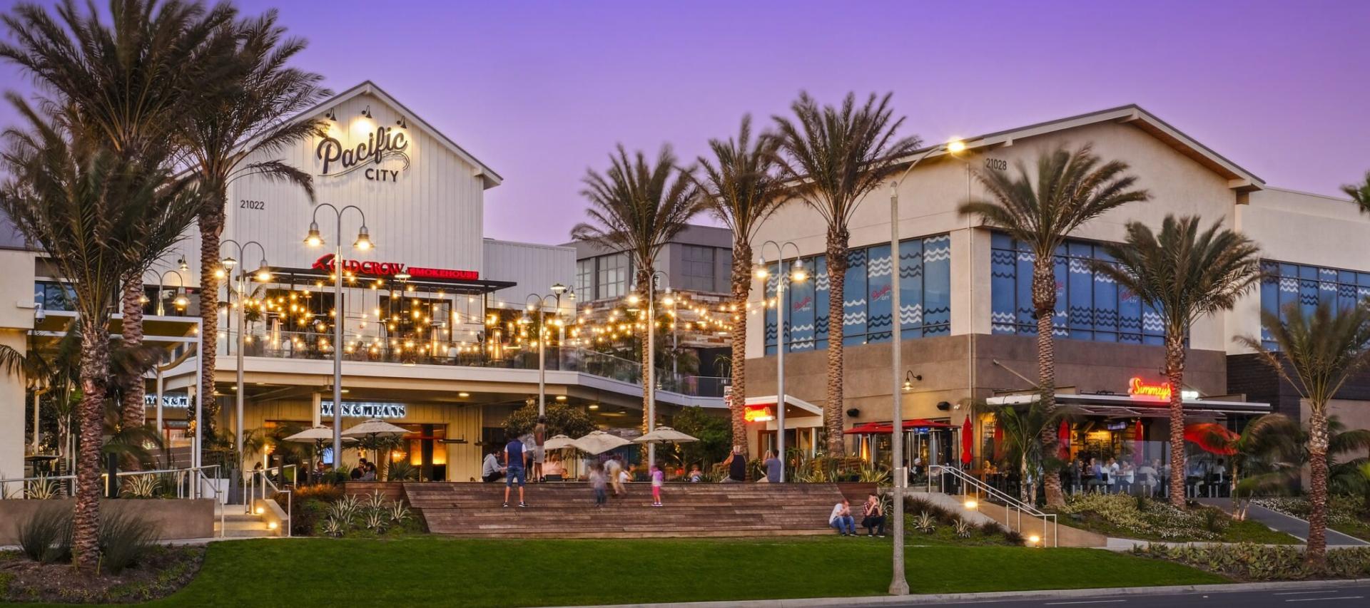 Exterior twilight photo of Pacific City shopping center in Huntington Beach, CA, with palm trees and a blue-purple evening sky