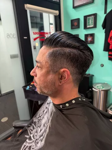 Man with a classic short side-parted hairstyle, wearing a black patterned barber cape, profile view