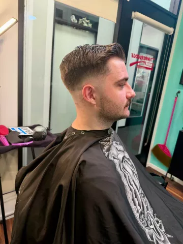 Man with a classic men's fade haircut, short on sides with length on top, wearing a black patterned cape