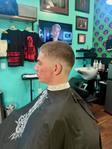 Man with a clean short taper haircut viewed from behind, wearing a black cape, teal barbershop background