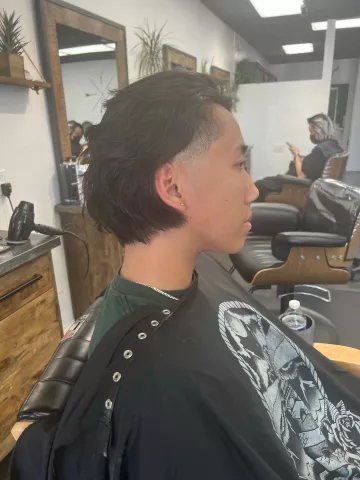 Man with a short skin fade haircut viewed from behind, wearing a graphic t-shirt, barbershop setting
