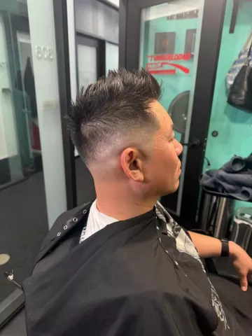 Man with a high skin fade haircut, short dark hair on top, wearing a black cape, profile view