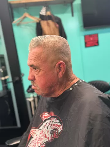 Older man with short silver-gray hair and a clean taper, wearing a black graphic barber cape, profile view