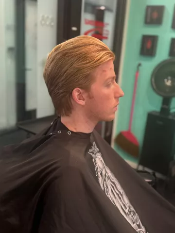 Man with auburn-toned swept-back hair and a tapered cut, wearing a black barber cape, profile view