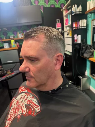 Older man with short silver hair and a fresh cut, wearing a vibrant graphic barber cape, profile view