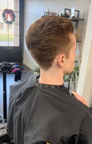 Young man with a short textured crop and clean tapered sides, wearing a black barber cape, viewed from behind in a barbershop