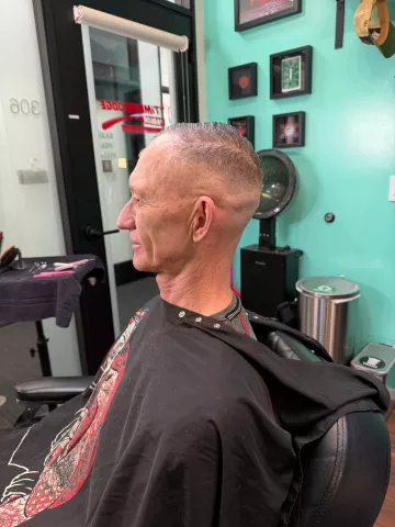 Senior man with a fresh fade haircut, seated in barber chair wearing a black cape, teal wall in background