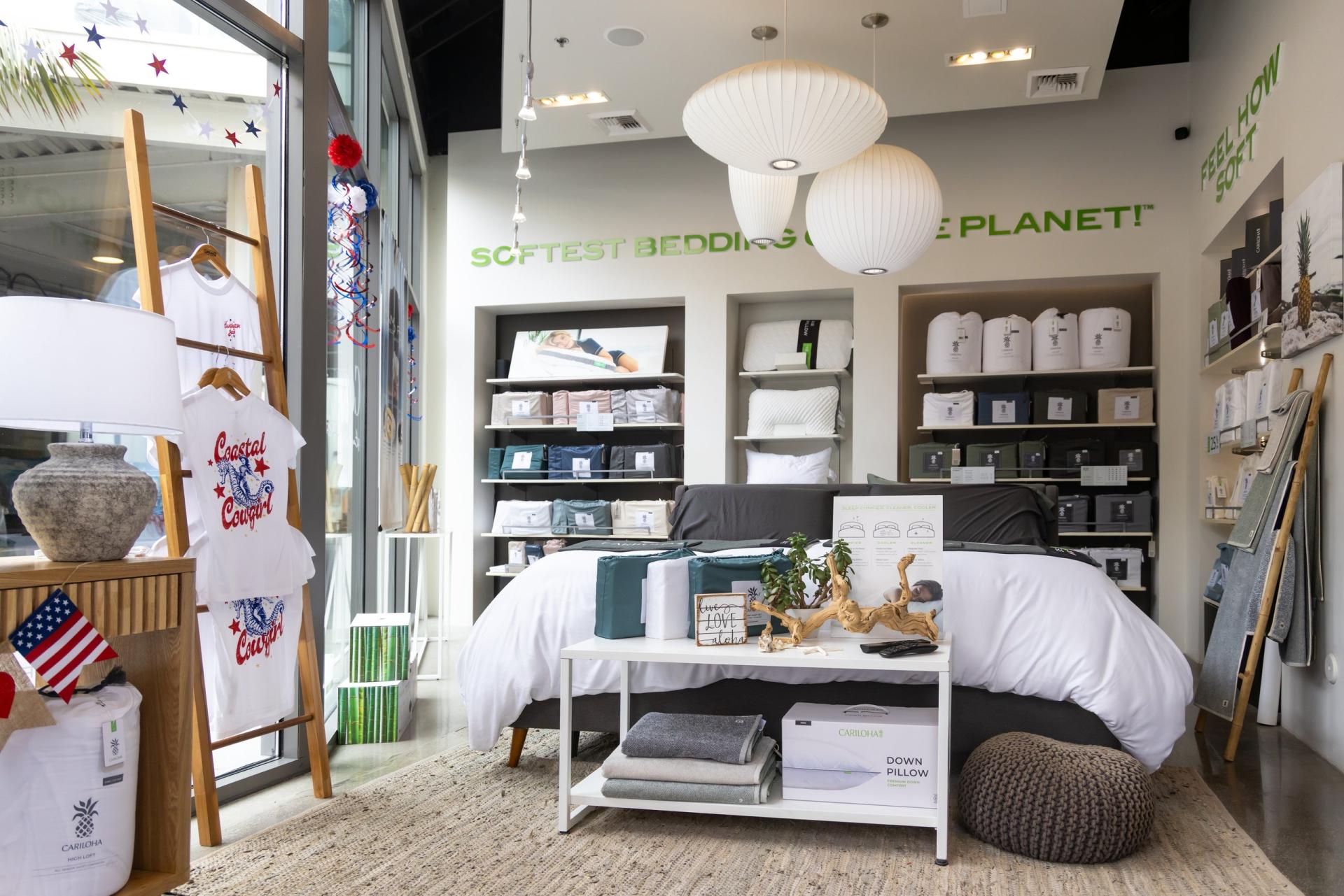 A made bed sits in front of shelves of pillows and sheet sets under the words "Softest bedding on the planet."