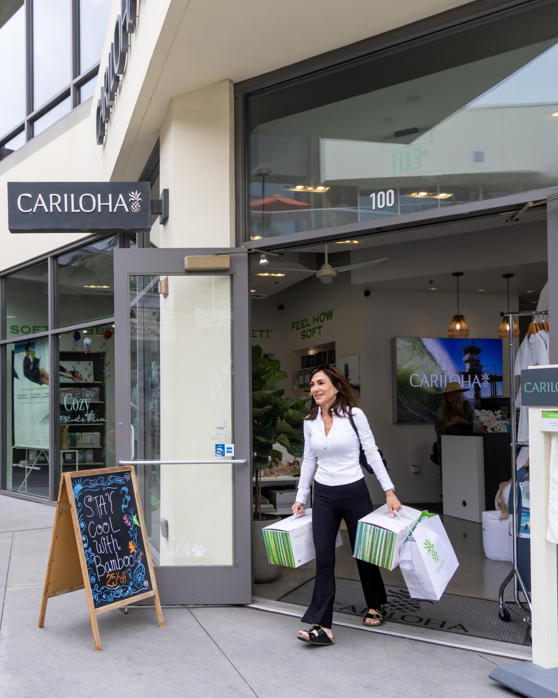 A shopper walks out of the Cariloha storefront at Pacific City carrying shopping bags past a chalkboard sign.
