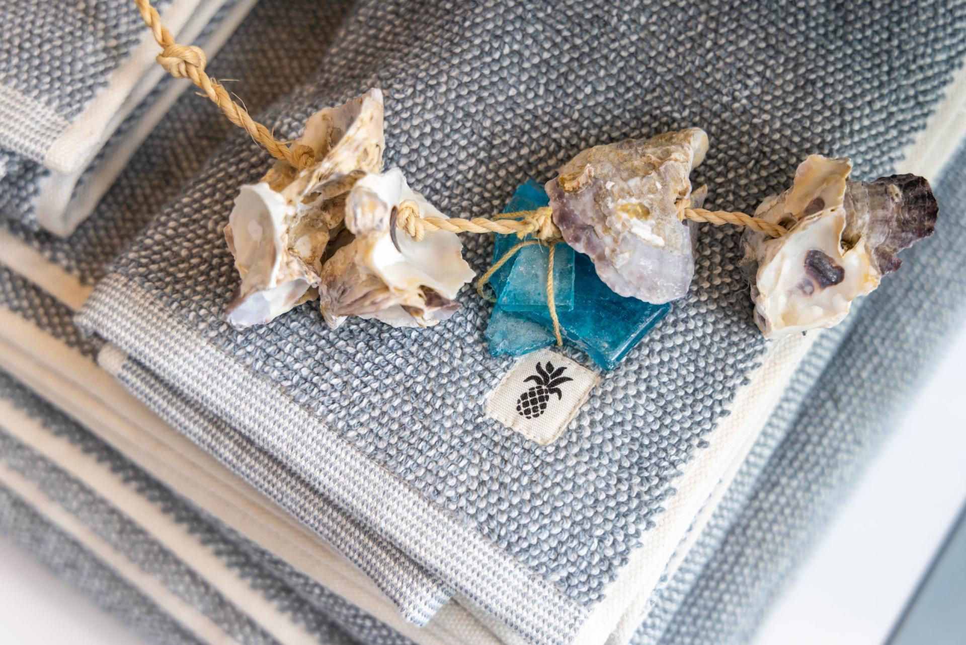 A string of shells and sea glass ties a stack of folded gray towels.