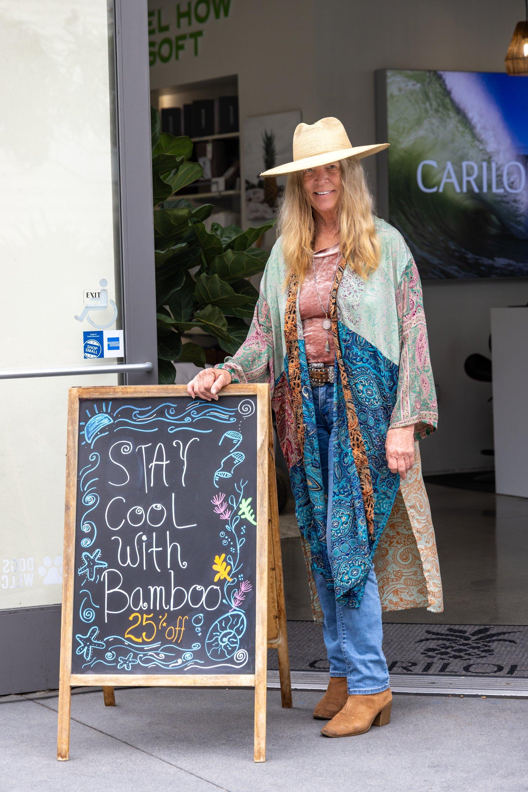A customer in a straw hat and a patterned kimono stands beside a chalkboard sign that reads "Stay cool with bamboo, 25% off."